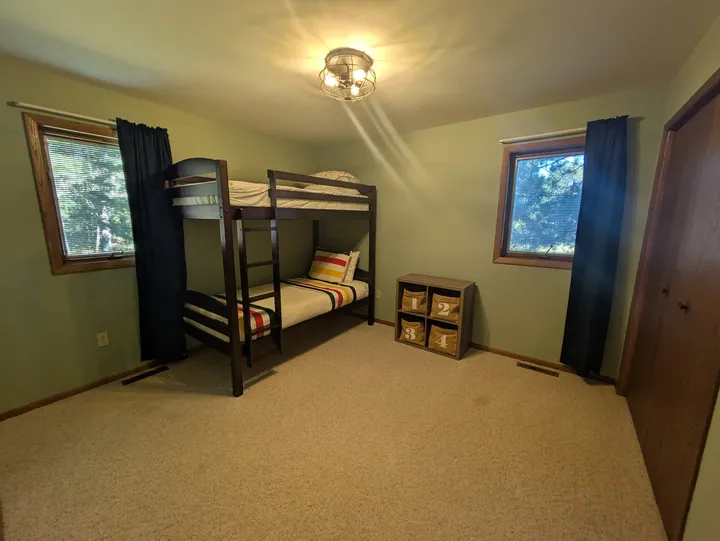Second main-level bedroom furnished with bunk beds and windows overlooking the trees