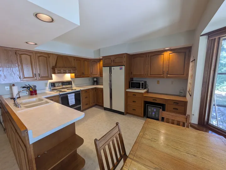 Wood cabinetry, peninsula and dining table beside the kitchen window