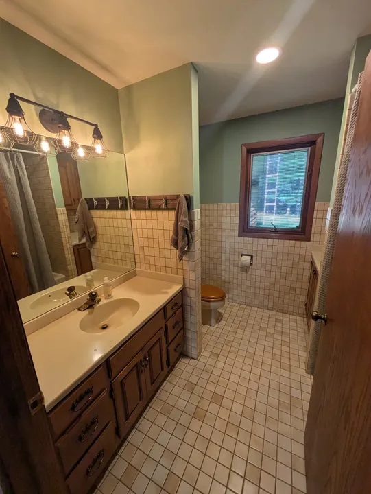Main-level guest bathroom with a wood vanity, mirror, tiled walls and window