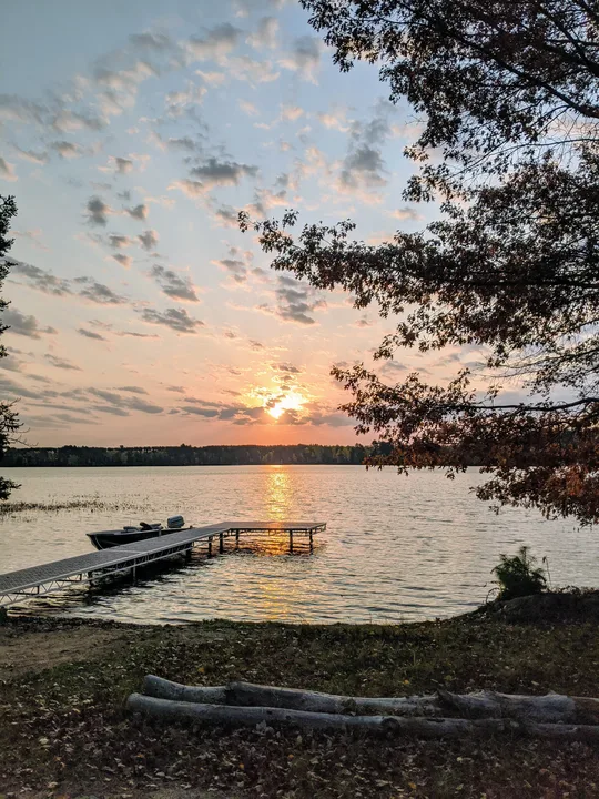 Sunrise over Snowden Lake with golden reflections beside the pier and a moored boat, framed by shoreline trees